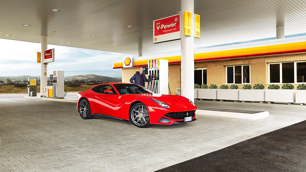 Ferrari rojo en una estación de servicio Shell con un hombre apoyado sobre un surtidor
