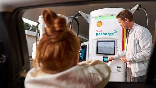 Un hombre usando una unidad de recarga Shell mientras una niña mira desde el interior de un automóvil