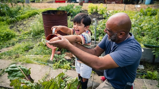 Hombre ayudando a un niño sonriente a regar plantas en un jardín