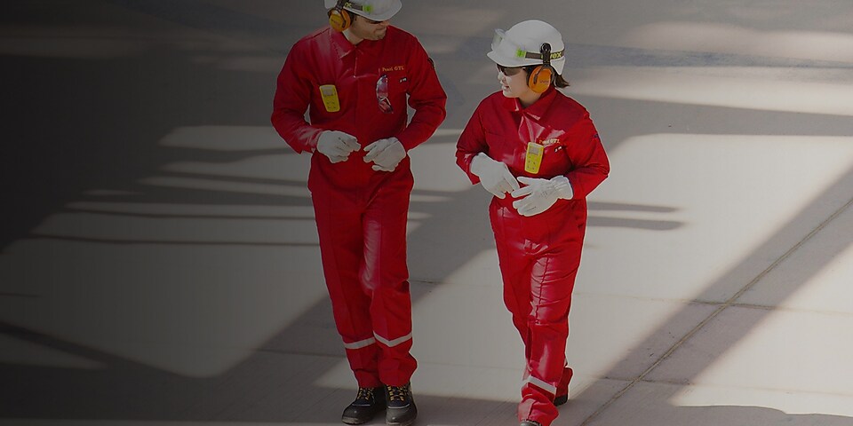 Trabajador y trabajadora con overoles rojos, cascos blancos y protección auditiva caminando