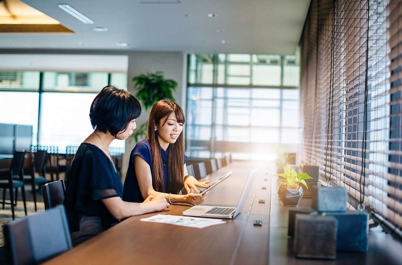 Dos mujeres sentadas en un escritorio mirando una computadora y una tableta