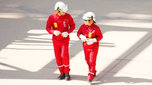Trabajador y trabajadora con overoles rojos, cascos blancos y protección auditiva caminando
