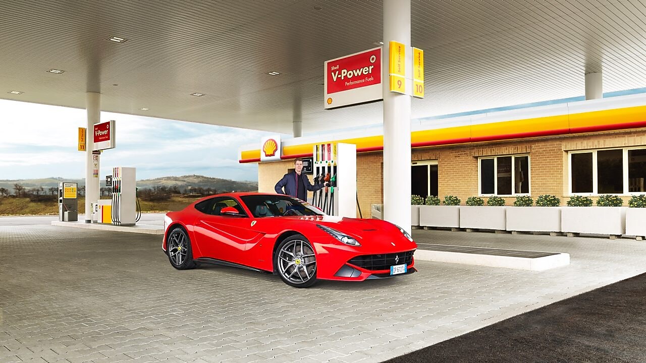 Ferrari rojo en una estación de servicio Shell con un hombre apoyado sobre un surtidor