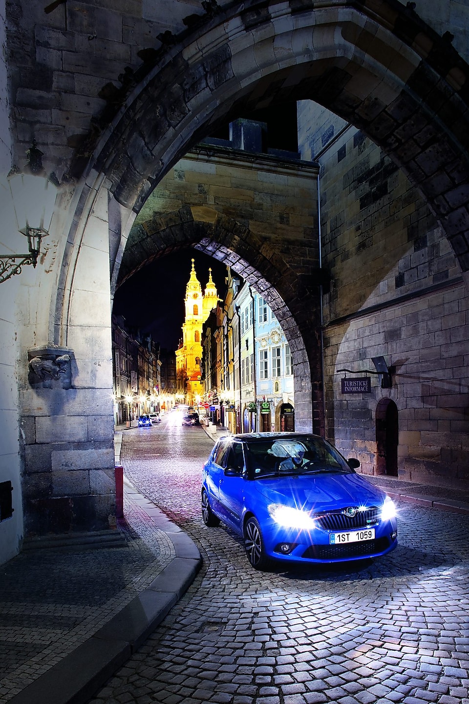 Auto azul aparcado bajo un arco en una calle empedrada de Praga de noche