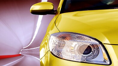 Parte frontal de un auto amarillo circulando por un túnel, con vista del faro delantero y el espejo lateral derechos