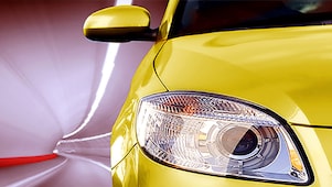 Parte frontal de un coche amarillo circulando por un túnel, con vista del faro delantero y el espejo lateral derechos