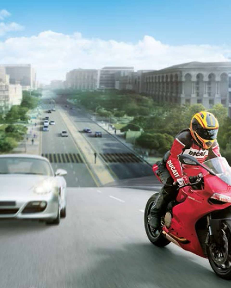 Motocicleta roja y piloto en una ruta con autos y edificios en el fondo